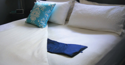 A neatly made bed with white sheets, the sheet is folded back to show the blue sensor pad that is used by Ageing In Place powered by Alarm.com to monitor the wellbeing of loved ones.